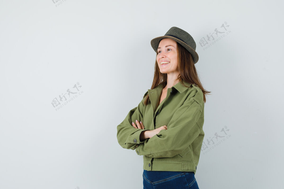 交叉穿着夹克 裤子 帽子 双臂交叉站着的年轻女士 看上去很高兴人类帽子女士