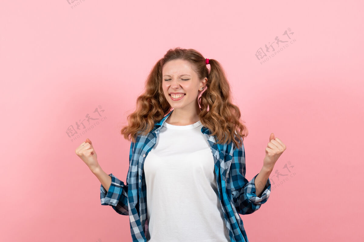 格子正面图：穿着格子衬衫的年轻女性在粉色背景上摆出姿势 欢欣鼓舞的造型 女人的情感 孩子的青春色彩姿势高兴漂亮