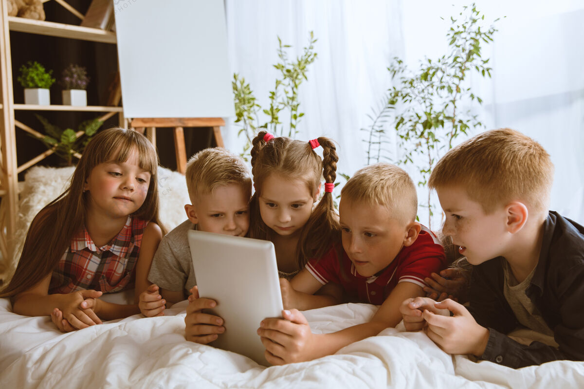小学生男孩和女孩在家里使用不同的小玩意孩子们带着智能手表 智能手机和耳机游戏男性现代