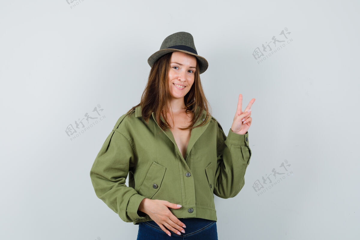 时尚穿着夹克 裤子 帽子的年轻女士 显示出v型标志 看起来很自信一起Vsign女性