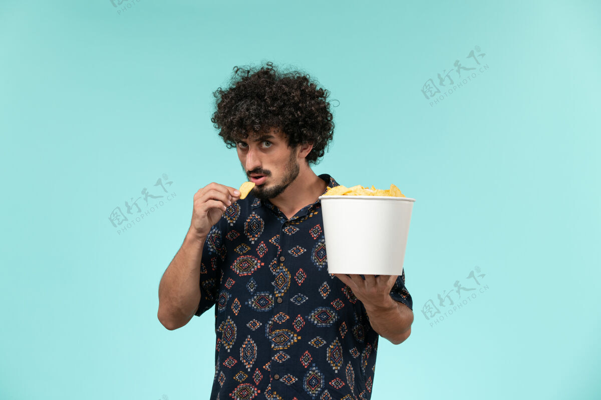 篮子正面图年轻人拿着篮子和土豆cips在蓝墙电影院吃电影男年轻人杯子咖啡杯