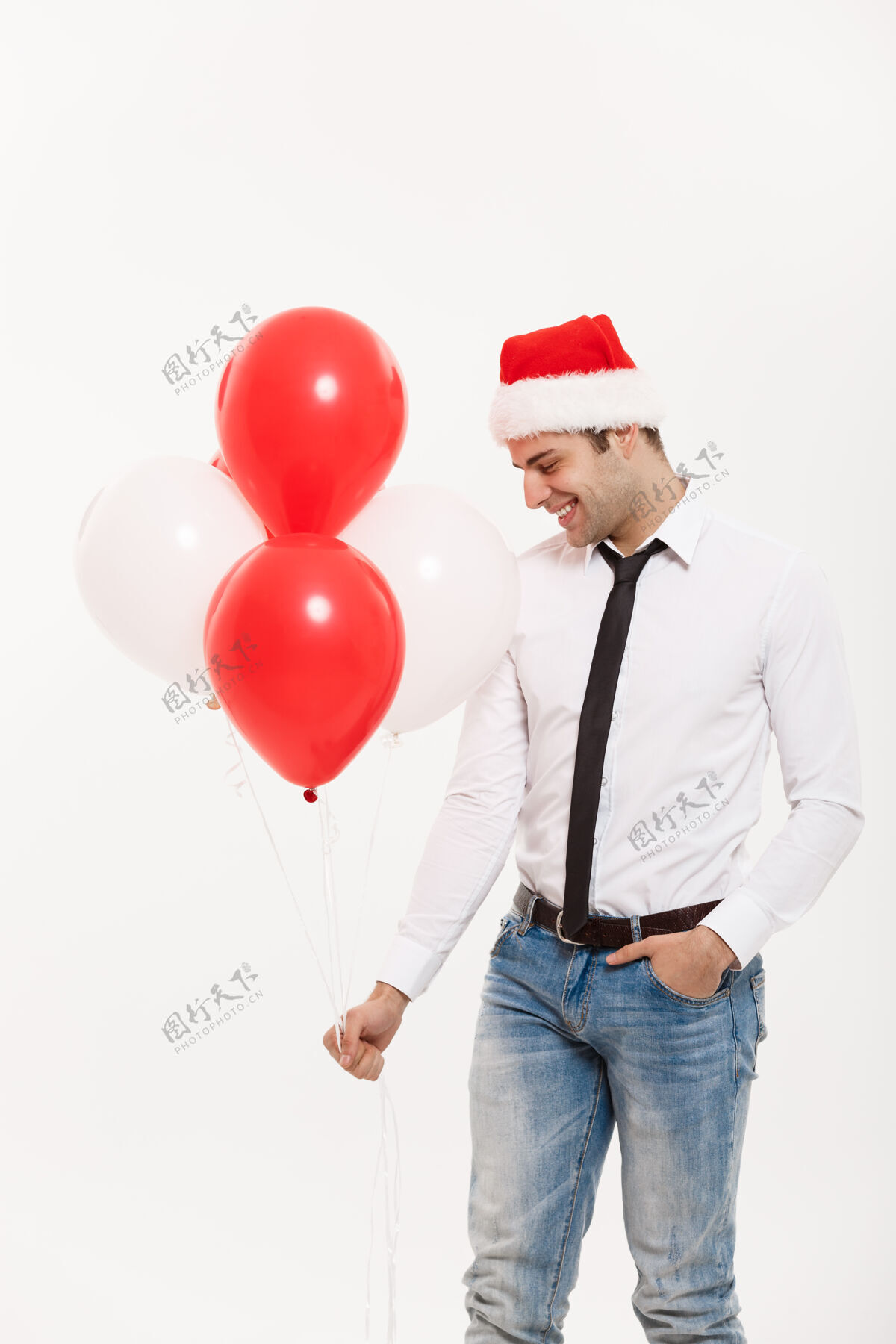 年轻帅气快乐的商务人士带着红气球散步 戴着圣诞帽庆祝圣诞快乐快乐成人圣诞节