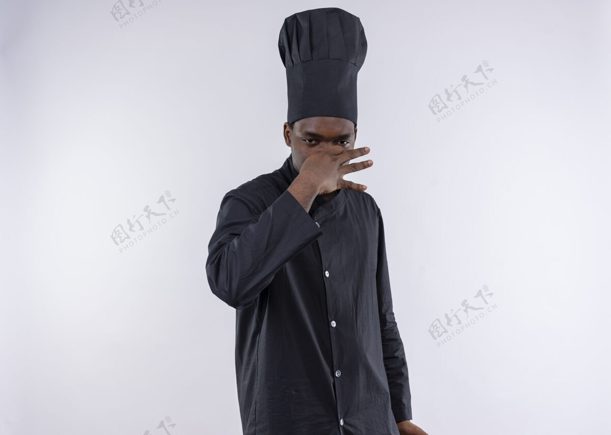 烹饪穿着厨师制服的年轻恼怒的美国黑人厨师用手捂住鼻子放在白色的地方鼻子厨师手