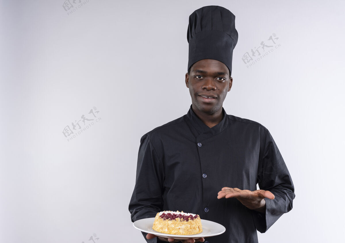 年轻身着厨师制服的年轻美籍黑人厨师手拿蛋糕放在盘子上 用手指着白色的空白处蛋糕非裔美国人持有