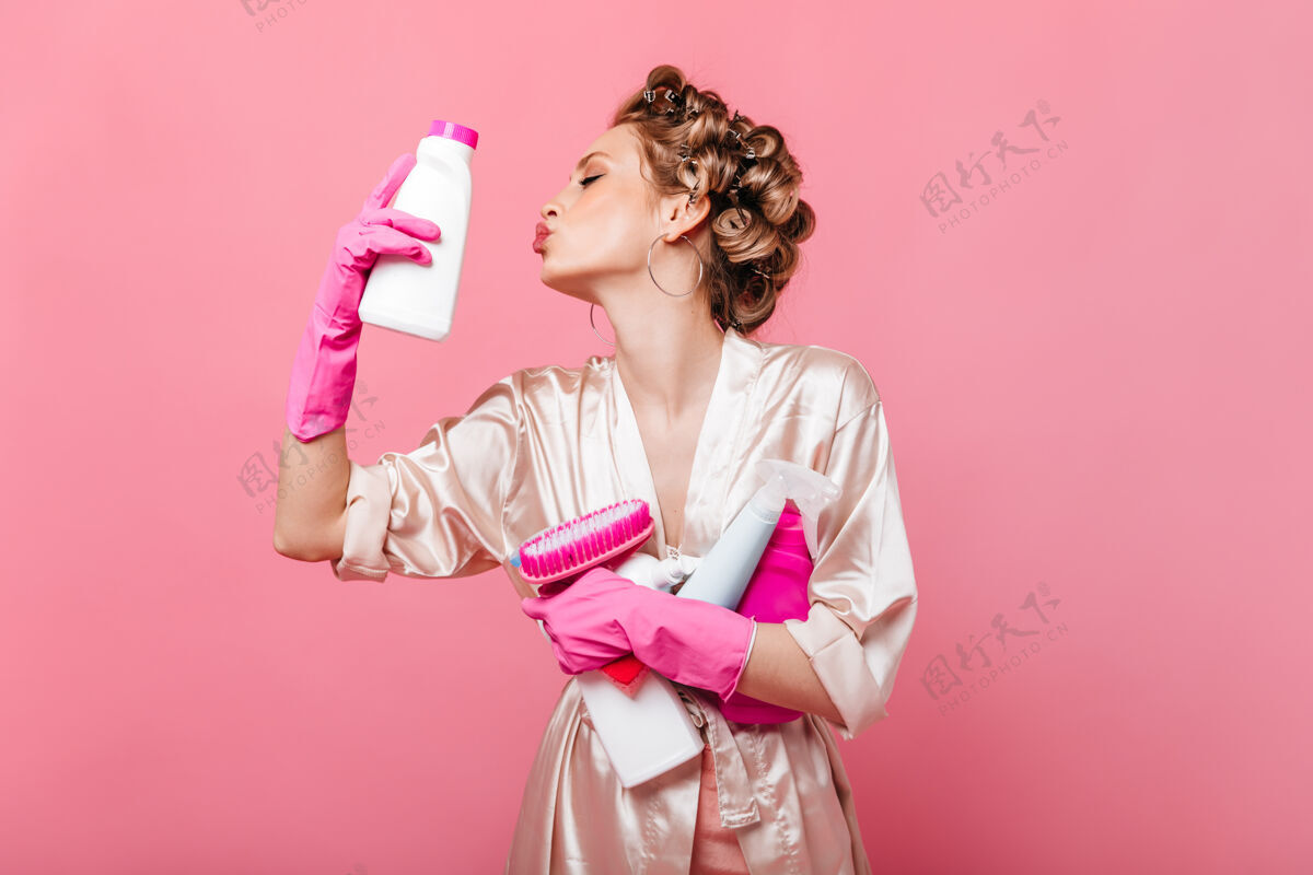 丝绸穿着浴衣的女人用洗涤剂在粉色墙上快乐地摆姿势的肖像年轻脸女性