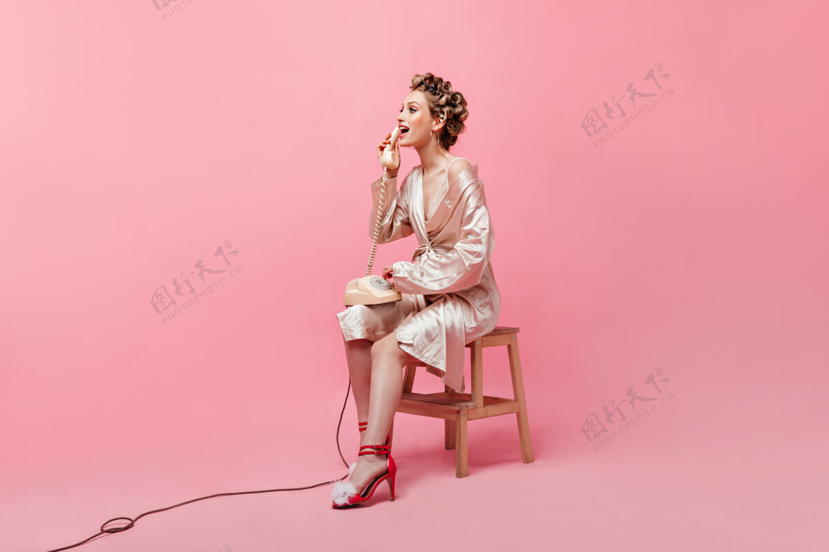衣服穿着粉红色长袍的漂亮主妇在隔离墙上动情地讲电话粉色浴袍长袍