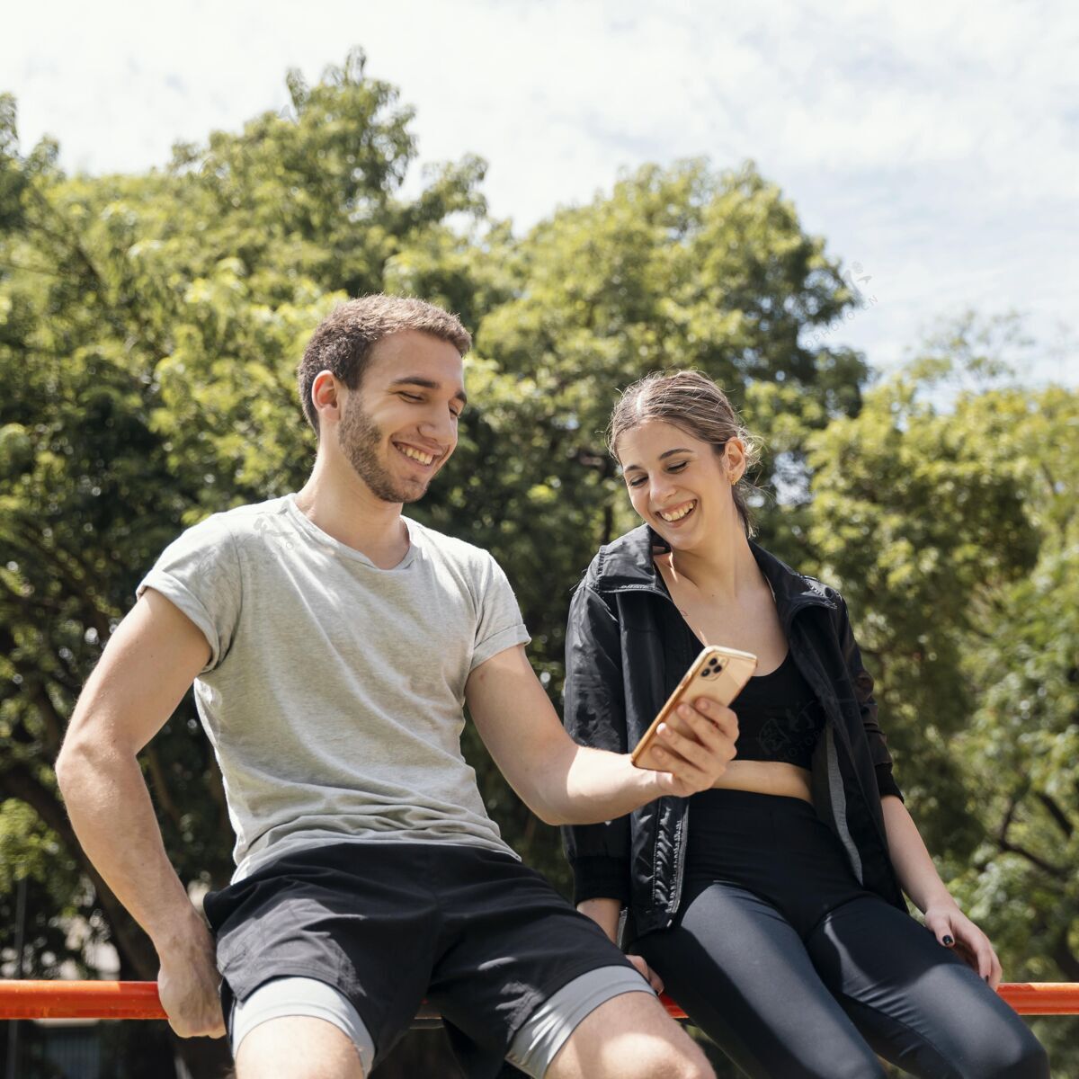 运动在户外运动时 带着智能手机的笑脸女人和男人运动锻炼活泼