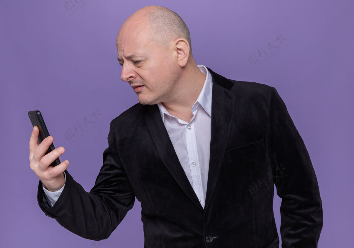 站着中年光头西装革履 手持手机 站在紫色的墙边 好奇地看着它西装电话阴谋