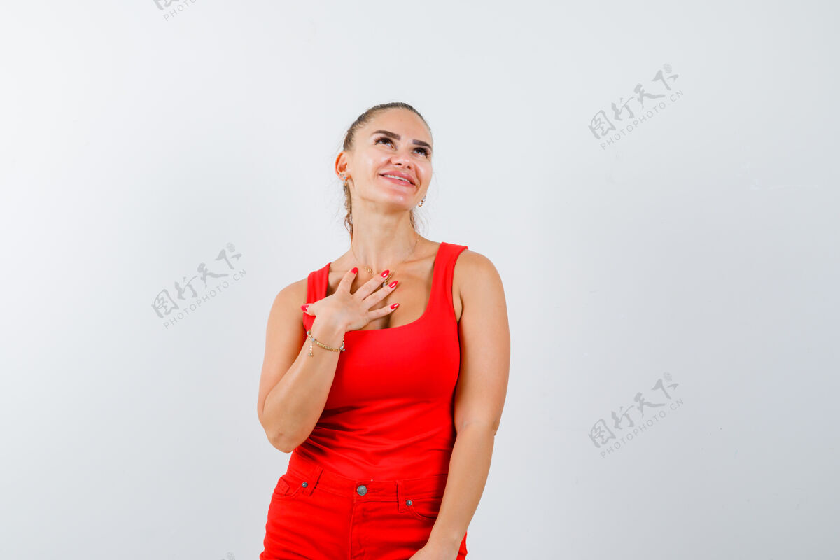 技术年轻女子手持手掌放在胸前的红色背心 裤子和看起来梦幻 前视图女性灵感人员