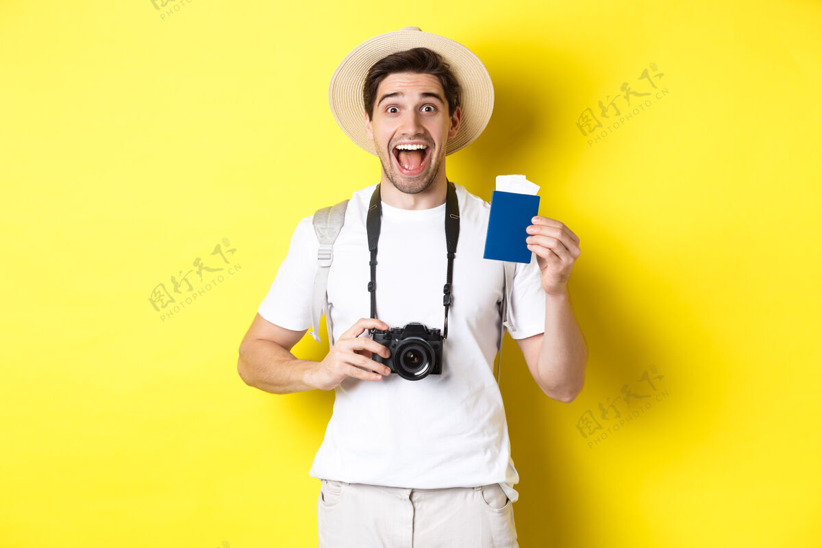 年轻人旅行 度假和旅游理念首先出示带票护照 手持相机 戴草帽 站在黄色背景上帅哥机票自信