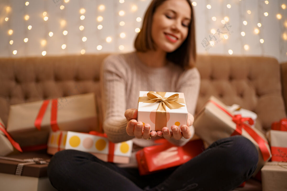 灯快乐的年轻女子抱着一个礼物展示被礼品盒环绕着盘腿坐着黑发辉光盒子