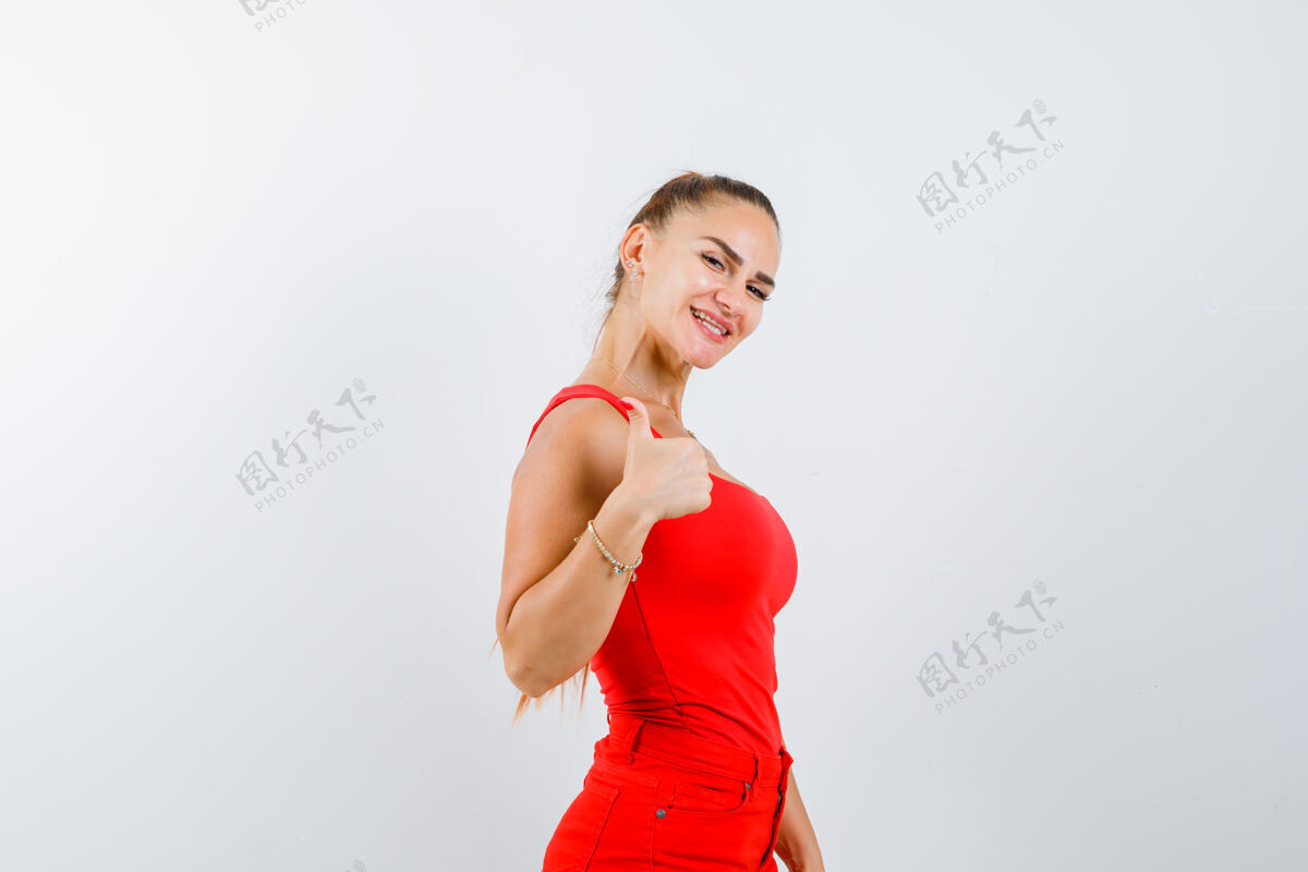 姿势年轻的女士在红色的单打 红色的裤子和看起来愉快的拇指向上 前视图季节享受裤子
