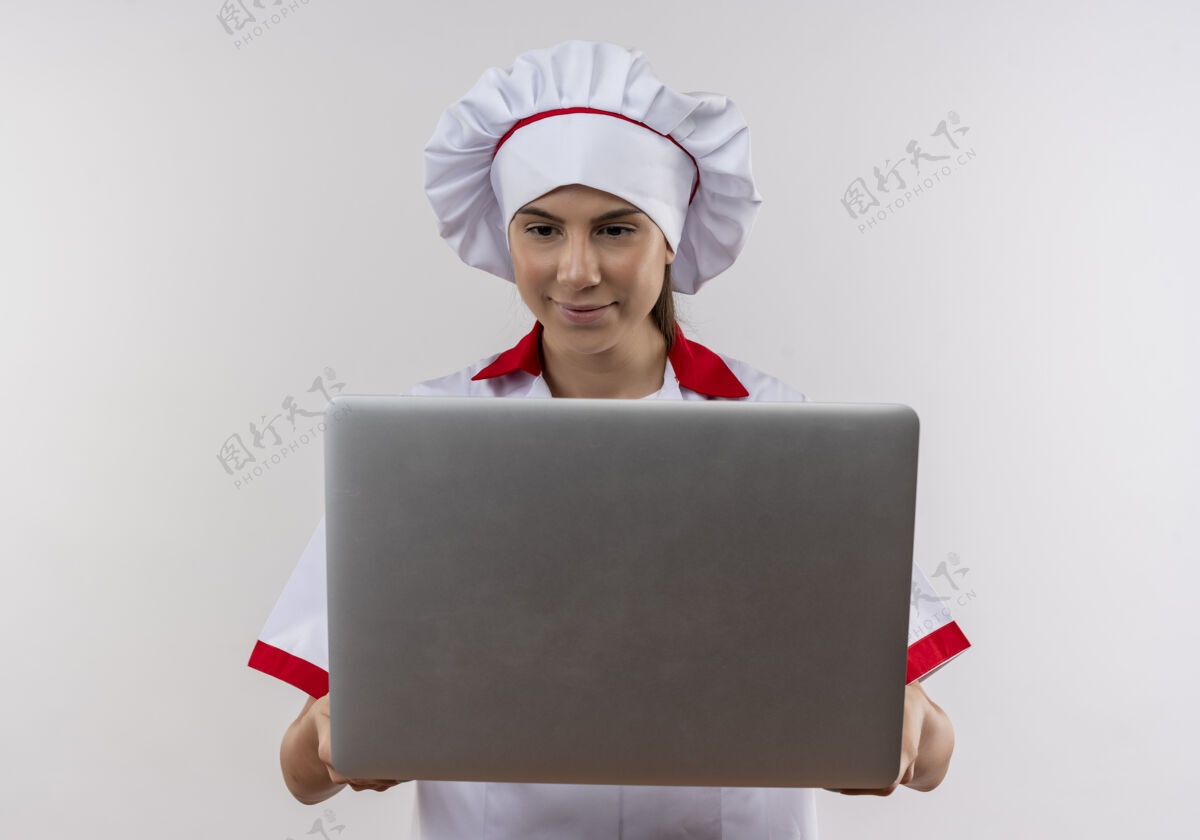 副本身着厨师制服的年轻高加索厨师女孩高兴地拿着并看着白色笔记本电脑上的复印空间空间烹饪请拿着