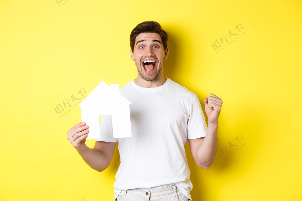 房子房地产概念兴奋的男子举行纸房子模型和庆祝 站在黄色背景快乐站着房地产男人