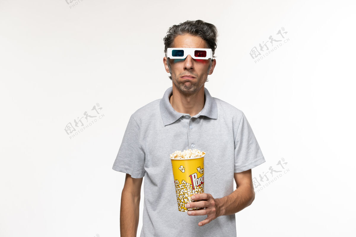 年轻男性正面图年轻男性戴着d型太阳镜在浅白色表面吃爆米花前面青少年太阳镜