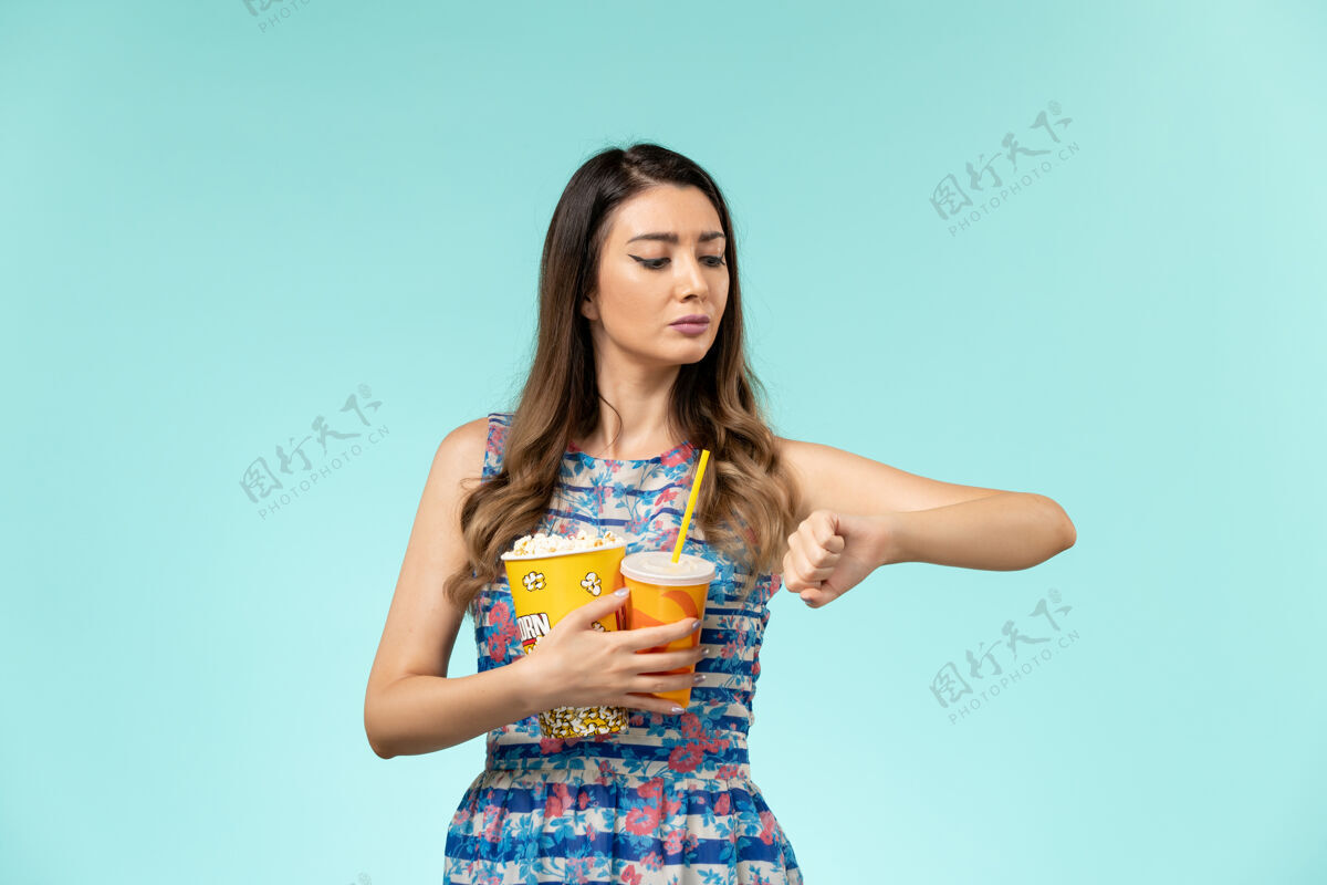 前面正面图年轻女子拿着爆米花喝酒看着她手腕上的蓝色表面爆米花年轻女性手腕