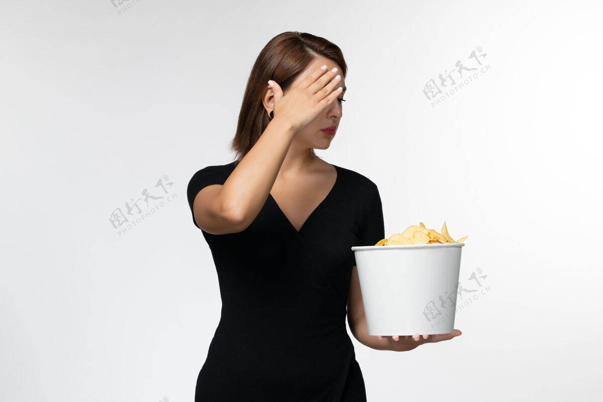 土豆正面图年轻的女性拿着篮子和薯片 在浅白色的表面上看电影电影院剧院浅白色