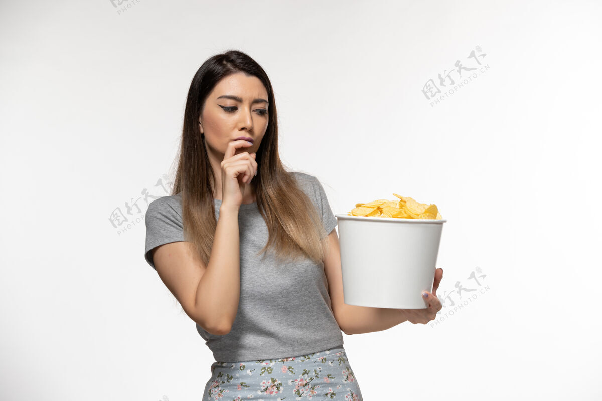 黑发正面图年轻女性在吃薯片看电影在浅白色的表面家庭主妇土豆孤独