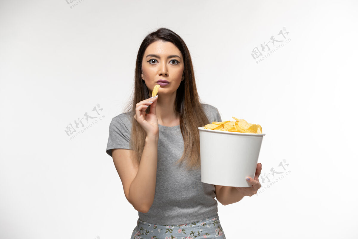 美丽正面图年轻女性在白色的表面上吃薯片看电影看孤独土豆