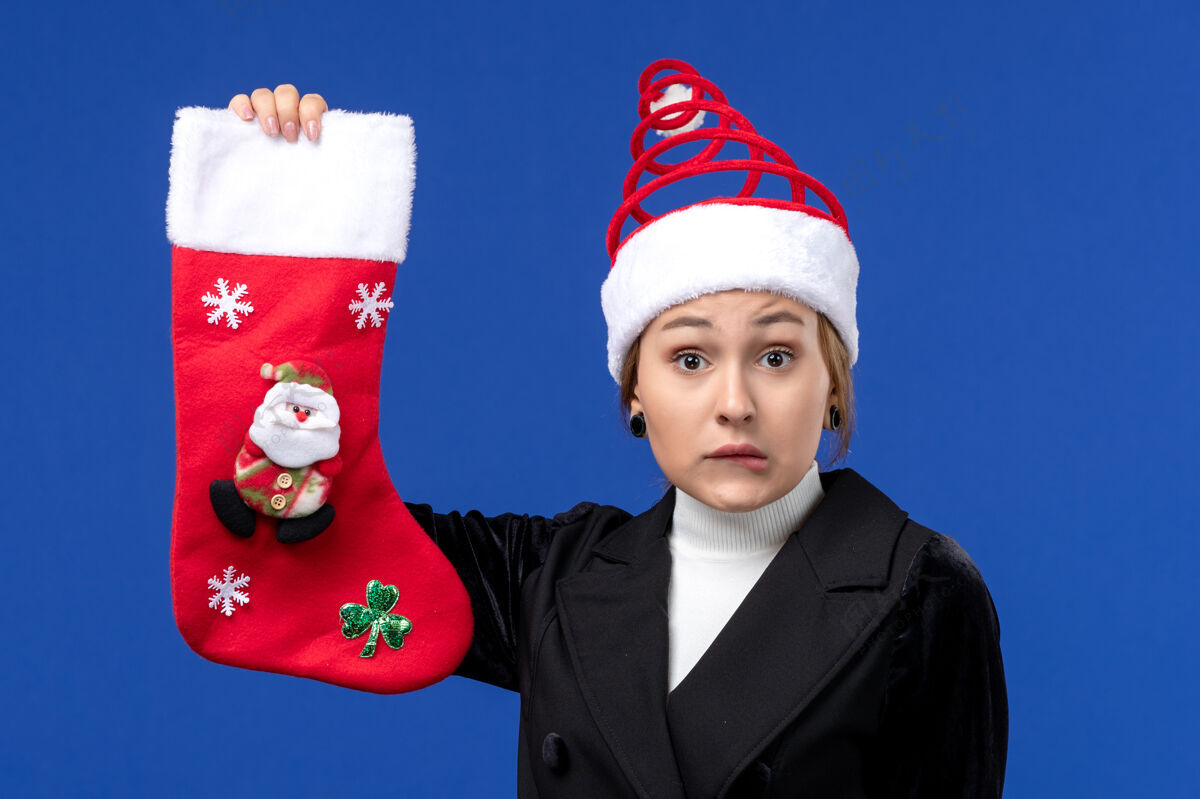 女人正面图：年轻女子拿着圣诞袜在蓝色墙壁上过年帽子庆祝欢乐