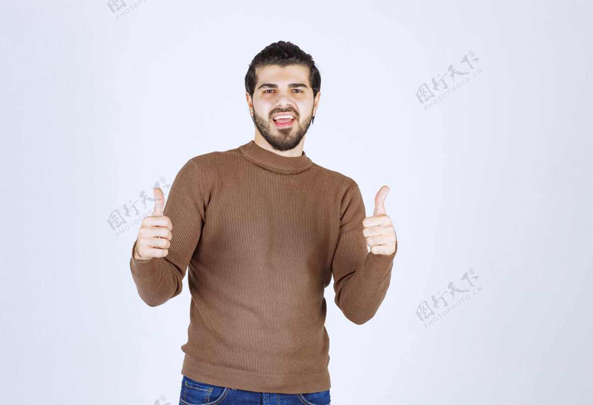 站立微笑的年轻人在白墙上竖起大拇指搞笑欢呼男性