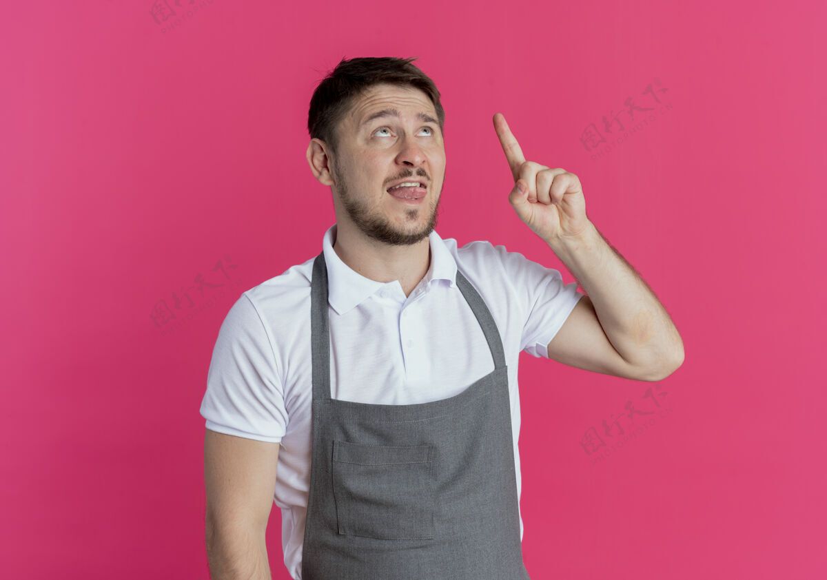 男人围裙上的理发师站在粉红色的墙上 用手指着头 有了新的想法手指站着理发师