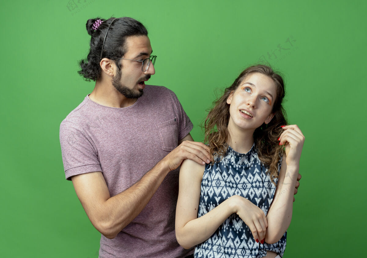 情侣一对年轻的男女 惊讶的男人抚摸着站在绿墙上沉思的女友的肩膀抚摸站男人