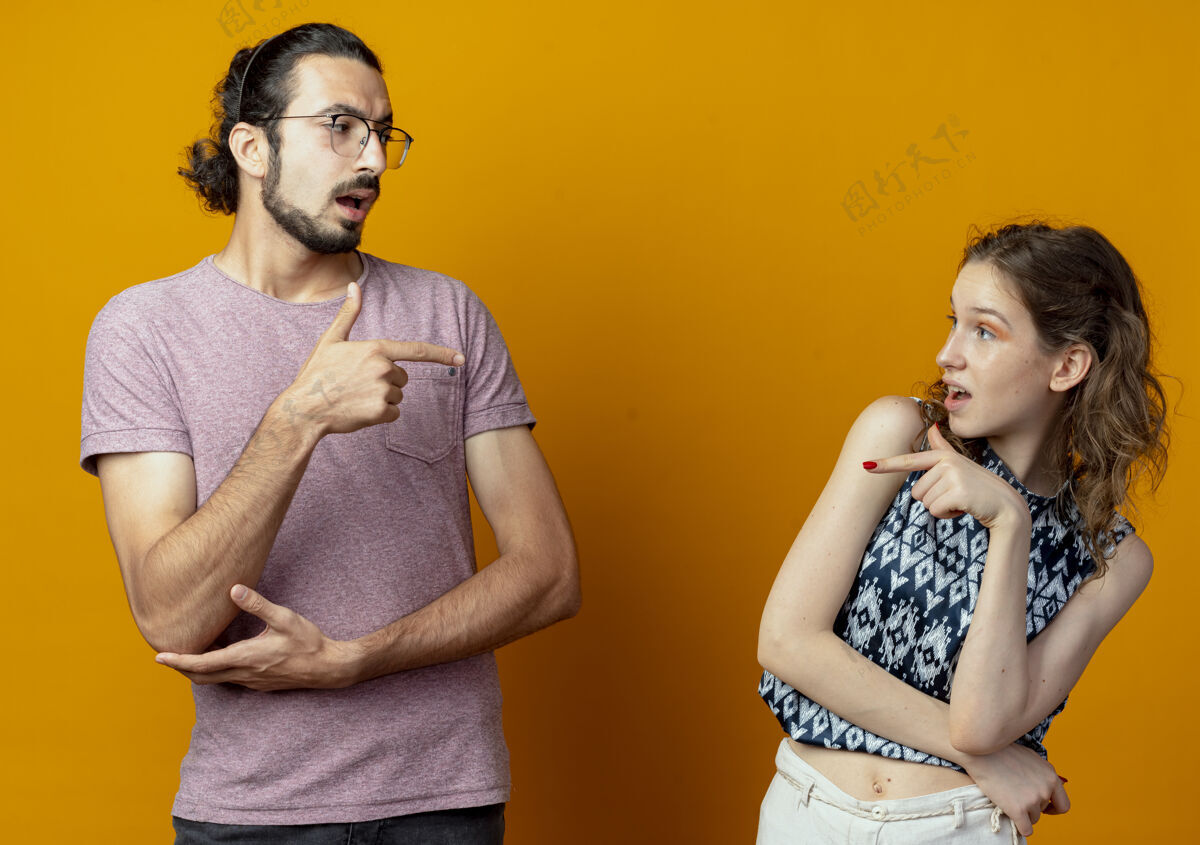 互相指责一对年轻夫妇在橘色的墙上互相指着对方吵架 互相指责男人夫妻吵架