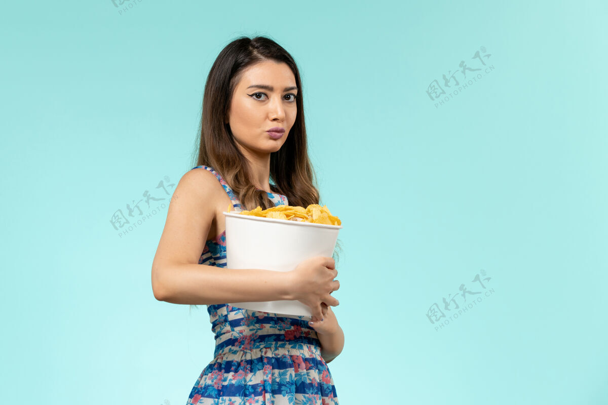 封面女郎正面图：年轻女性拿着蓝色桌子上的芯片包黑发女前面