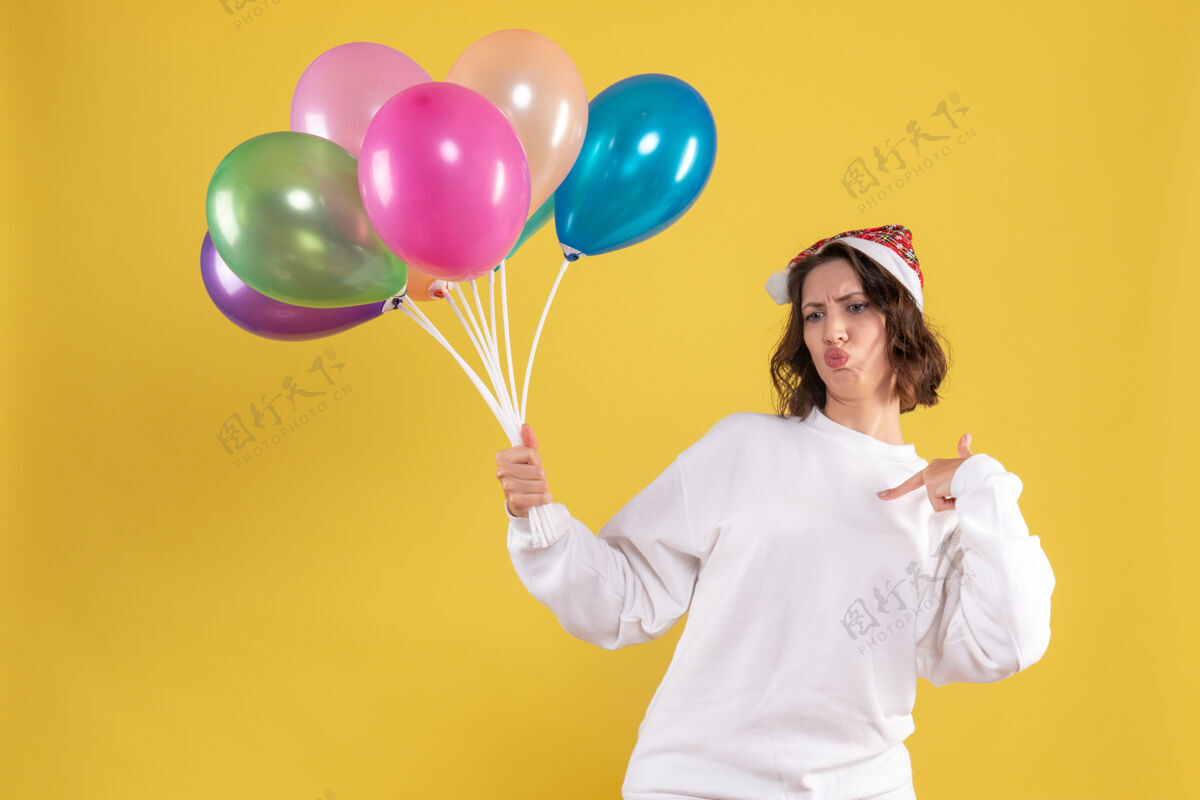 庆祝正面图年轻靓女手持气球对一位黄色圣诞新年彩女感慨不已吹气球颜色
