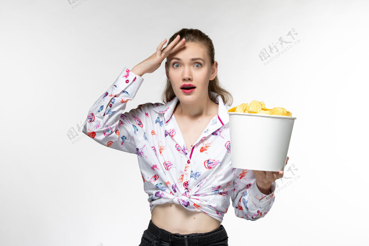 看正面图：年轻的女性拿着土豆片的篮子在浅白色的表面上看电影女士电影漂亮