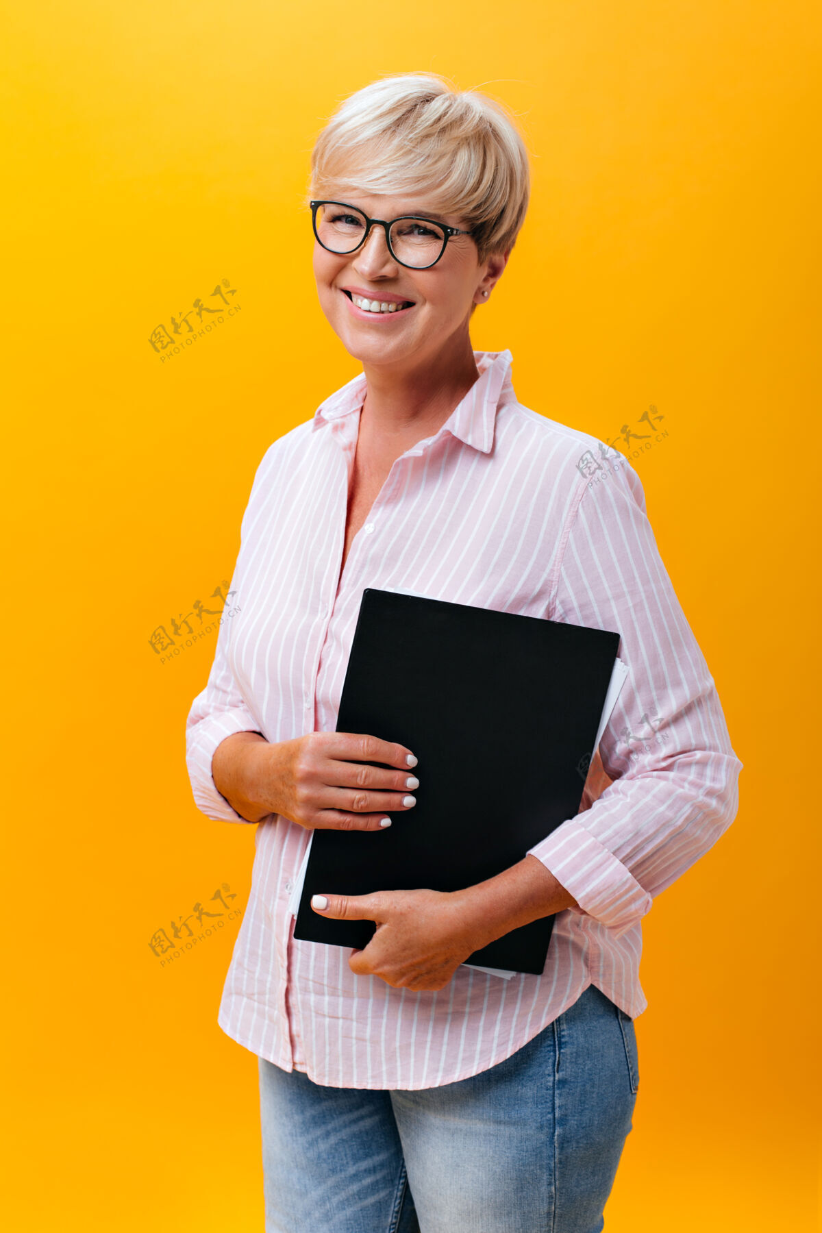 年穿着牛仔裤 粉色衬衫 戴着眼镜的酷女人摆出橙色背景上的纸片造型50多岁成人中年