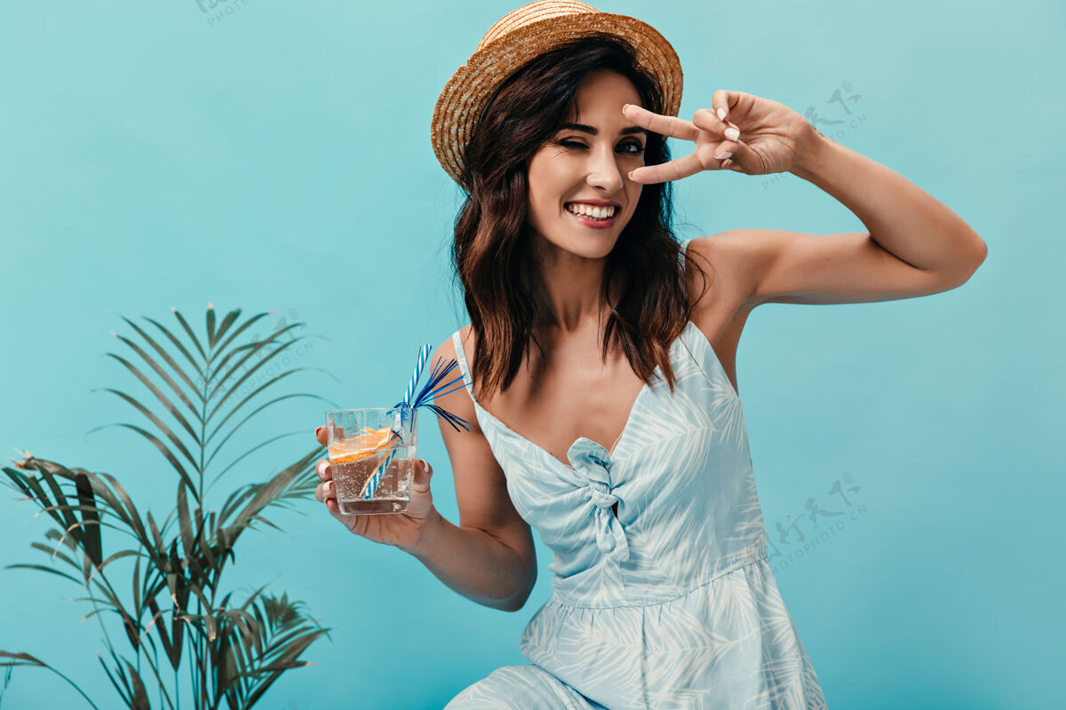 衣服可爱的女孩展示和平的标志 眨眼 拿着桔子喝水微笑的女人 黑色短发 在小棕榈树旁摆姿势闹钟衬衫思考
