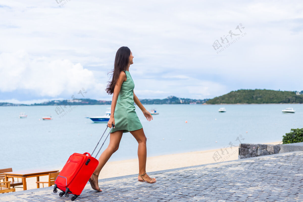 时尚快乐的白种人漂亮的长发优雅的旅游女人在酒店外面穿着红色的手提箱女人行李年轻