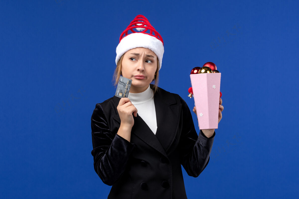 银行前视图：带着圣诞树玩具和银行卡的年轻女士在蓝色墙壁上过年西装人女人