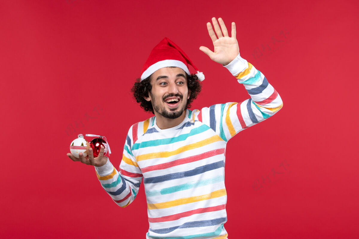 看法正面图年轻人拿着圣诞树玩具在红墙假日红人新年玩具前面球员