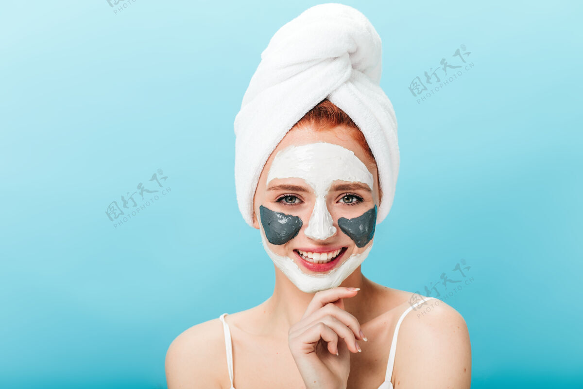 面部戴着面具的幸福高加索女人的正面图可爱女孩头戴毛巾在蓝色背景下摆姿势的摄影棚照片微笑无忧无虑面部