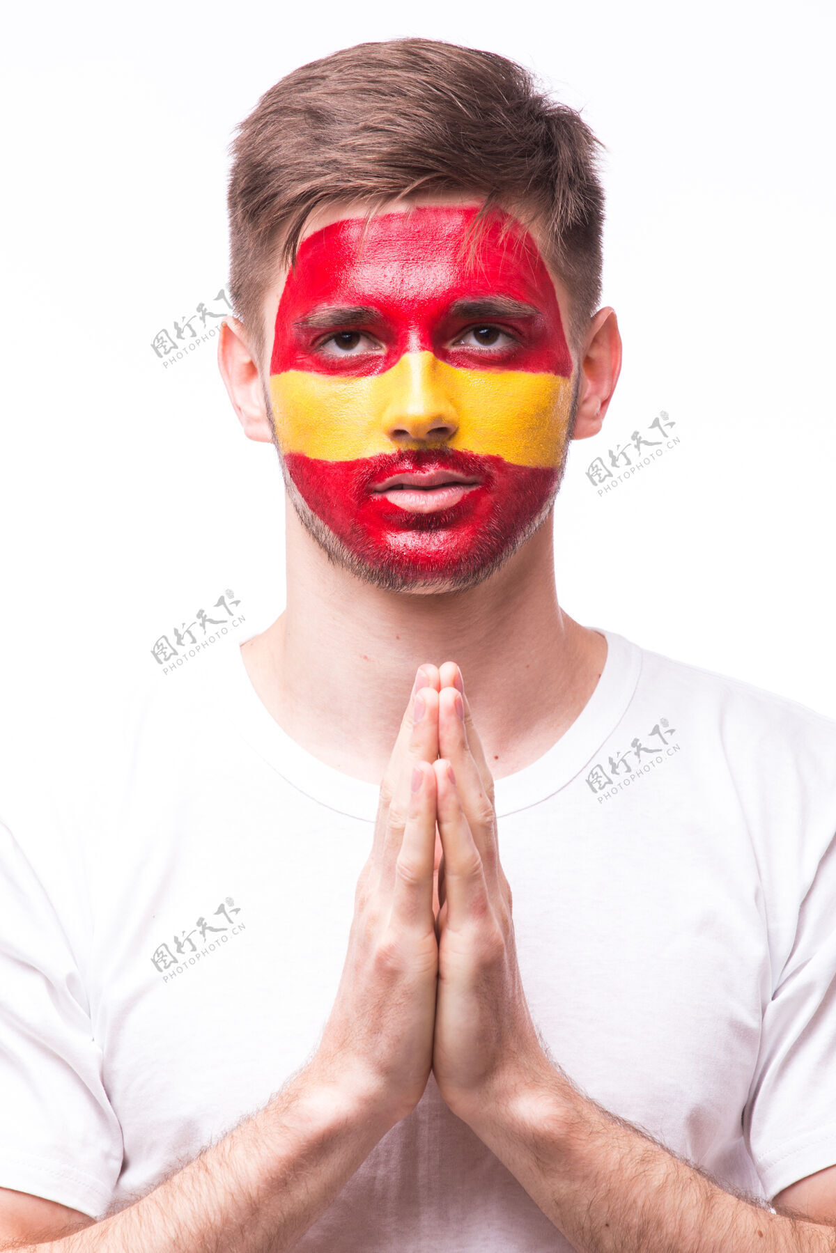 男人年轻的西班牙男足球迷用祈祷的手势孤立在白墙上男性国旗足球