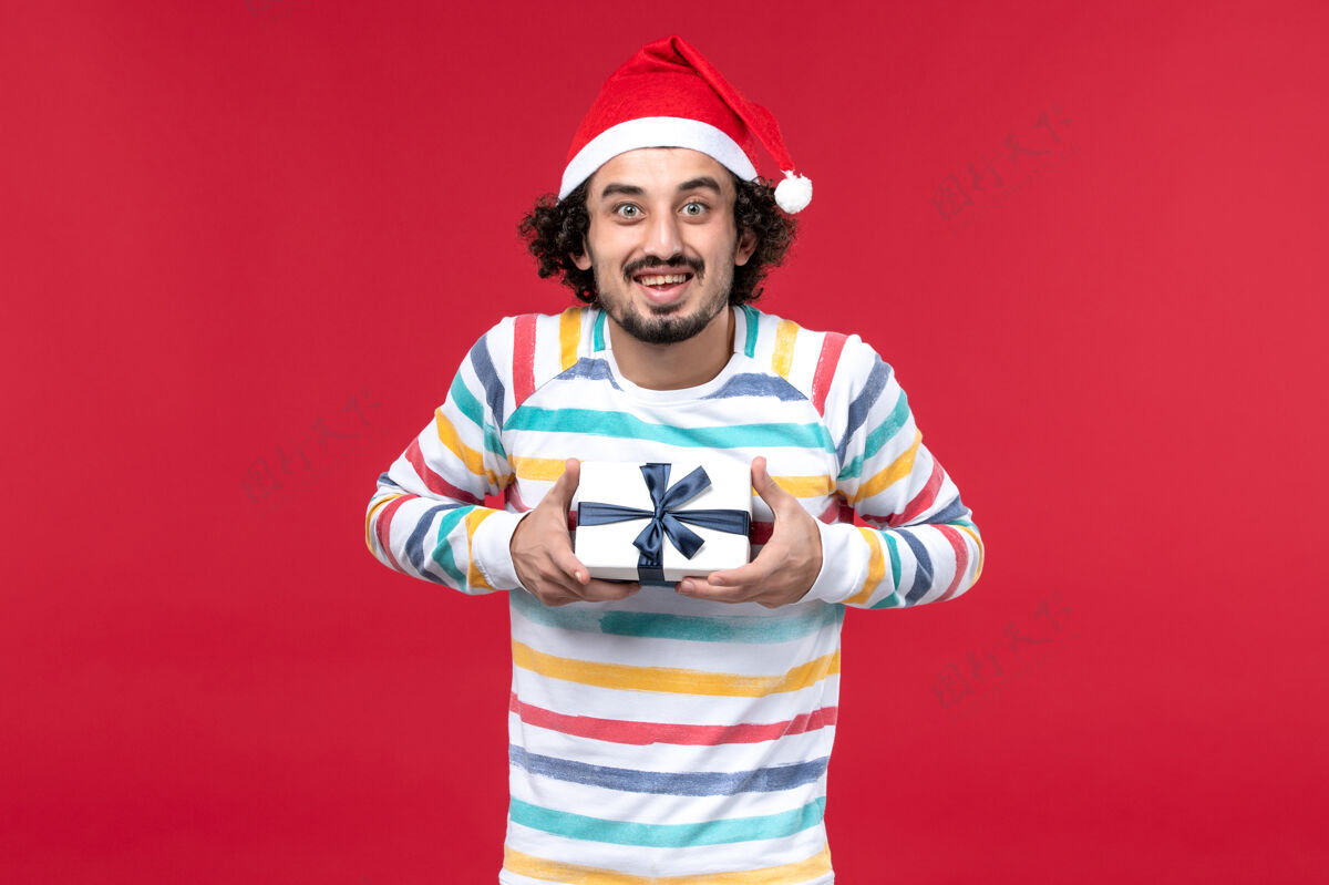 男性正面图年轻男性手持新年礼物在红色背景节日红色新年年轻男性圣诞节休闲