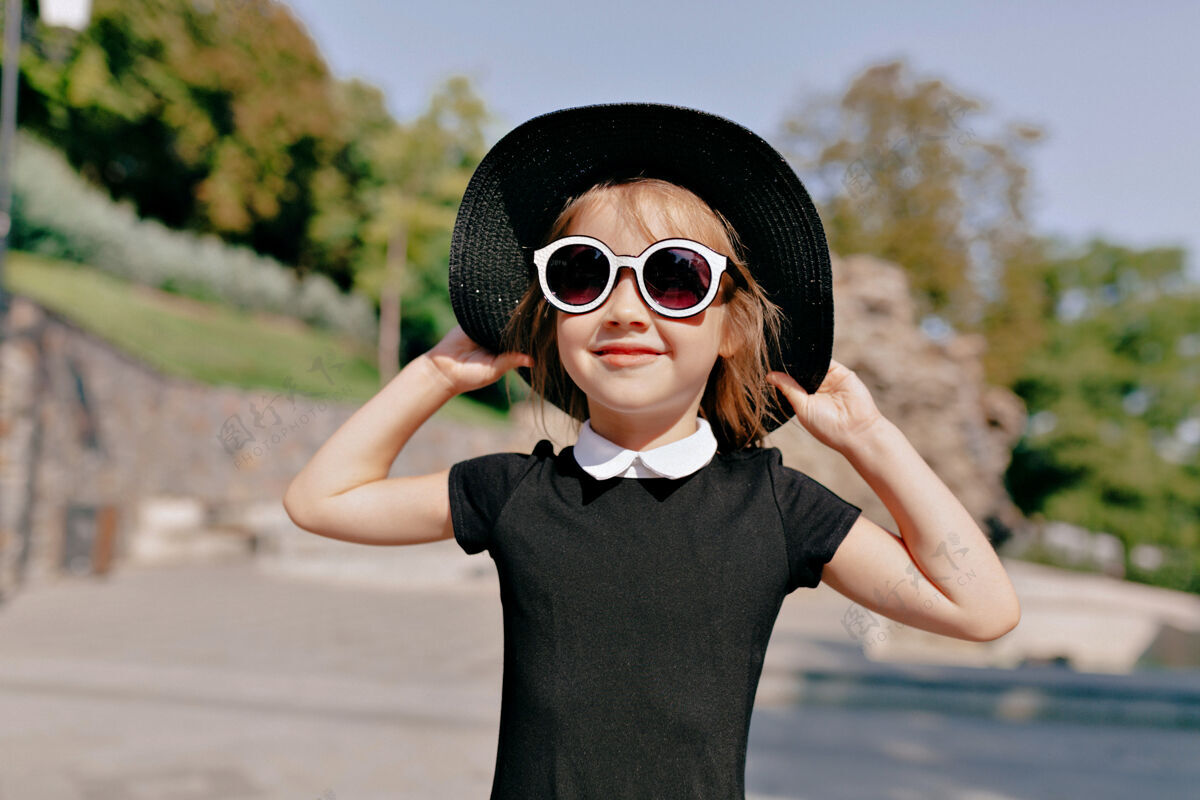 享受可爱可爱的小女孩戴着帽子和太阳镜在阳光明媚的温暖的日子里漫步在公园里时尚时尚帽子
