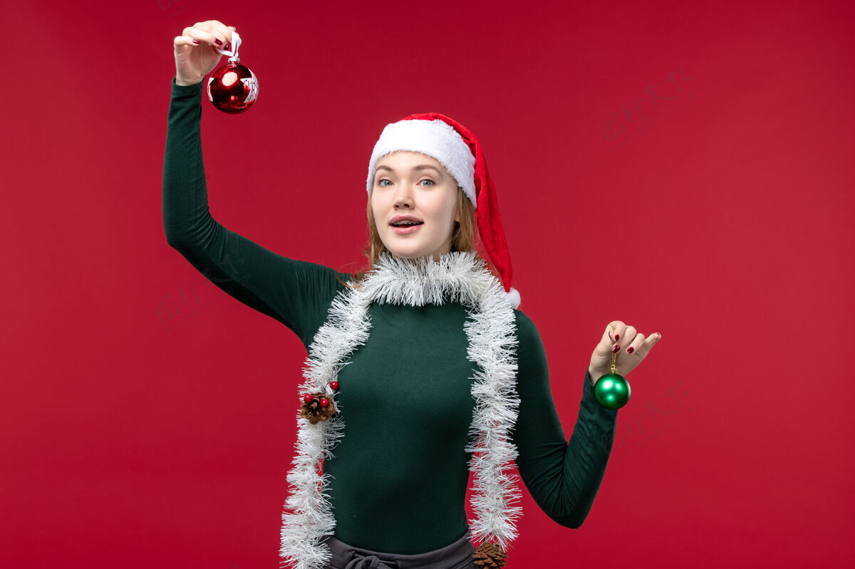 圣诞节正面图红色背景上手持圣诞树玩具的年轻女性正面肖像风景