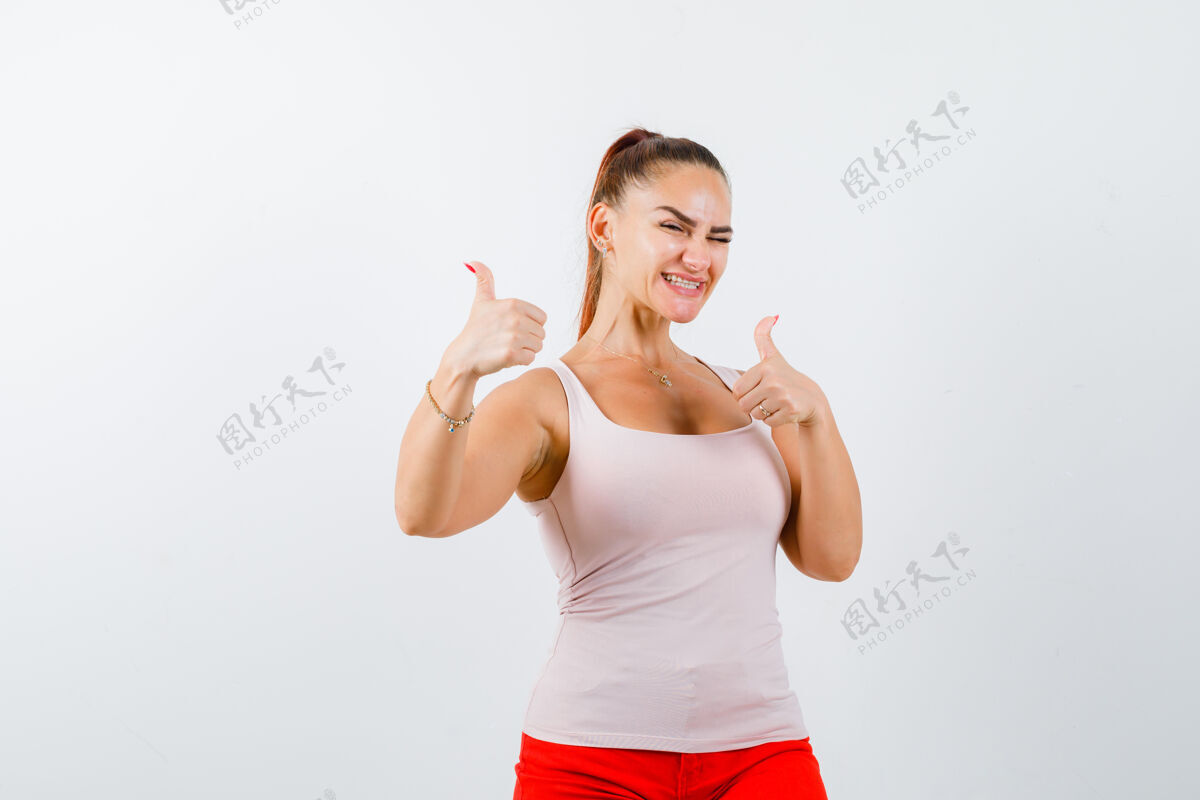 人穿着米色上衣和红色裤子的年轻女孩向上竖起大拇指 看上去很自信快乐头发裤子