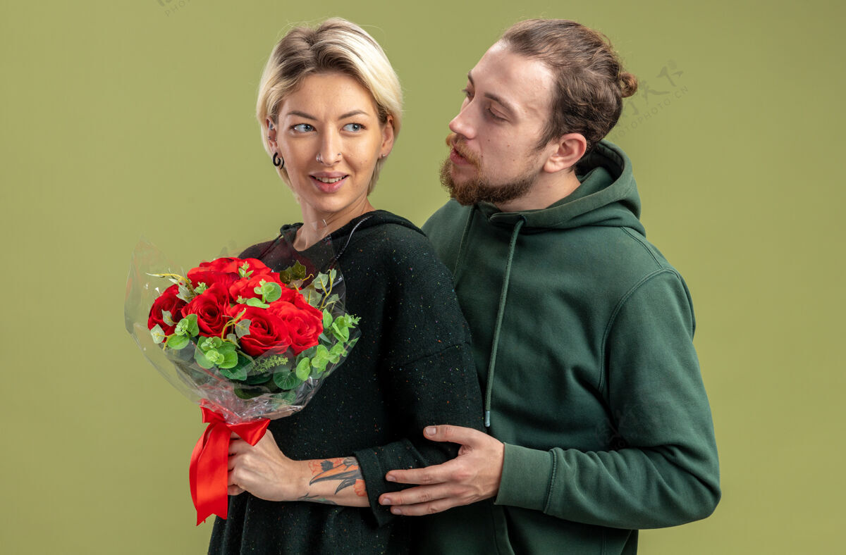 衣服一对穿着休闲服的年轻夫妇幸福地拥抱着他可爱的女人 带着鲜花站在绿色的墙上庆祝情人节爱情情人节情侣