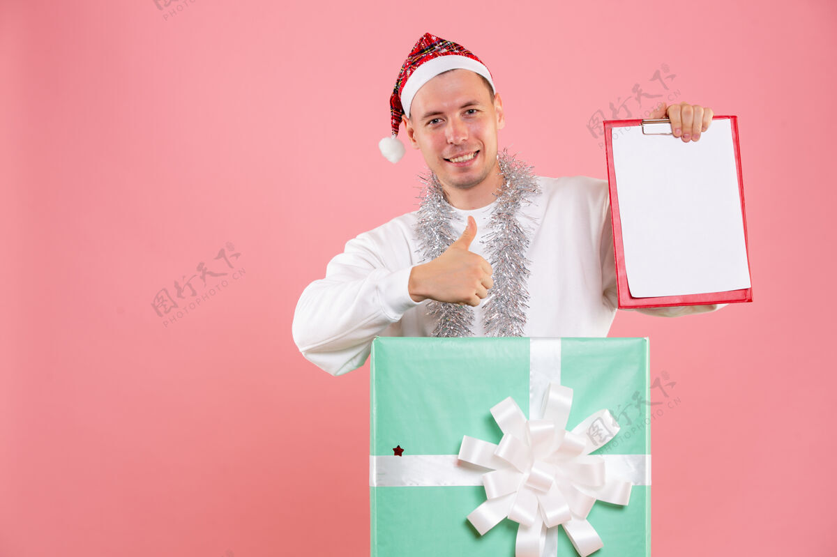 视图正面图：年轻男性在粉红色背景下拿着文件笔记文件睡衣圣诞