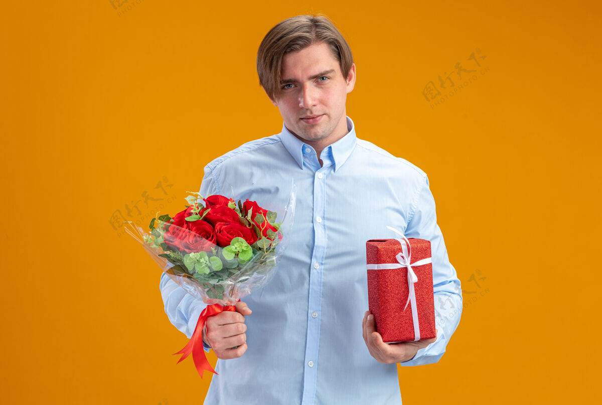 男人身穿蓝衣的男子手持一束红玫瑰 站在橙色的墙上 看着相机微笑着自信的情人节概念微笑花束立场