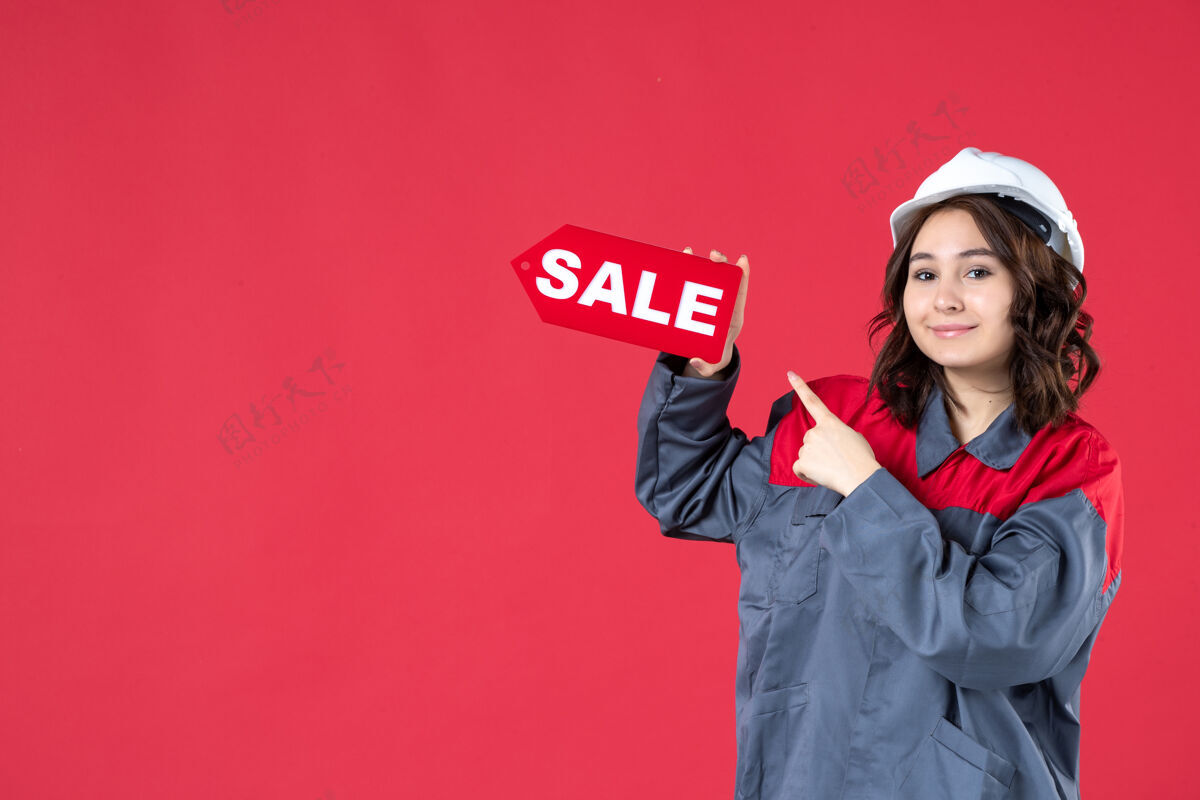 尖正面近景：身着制服 戴着安全帽 指着隔离红墙上的销售图标 面带微笑的女工女工微笑前面