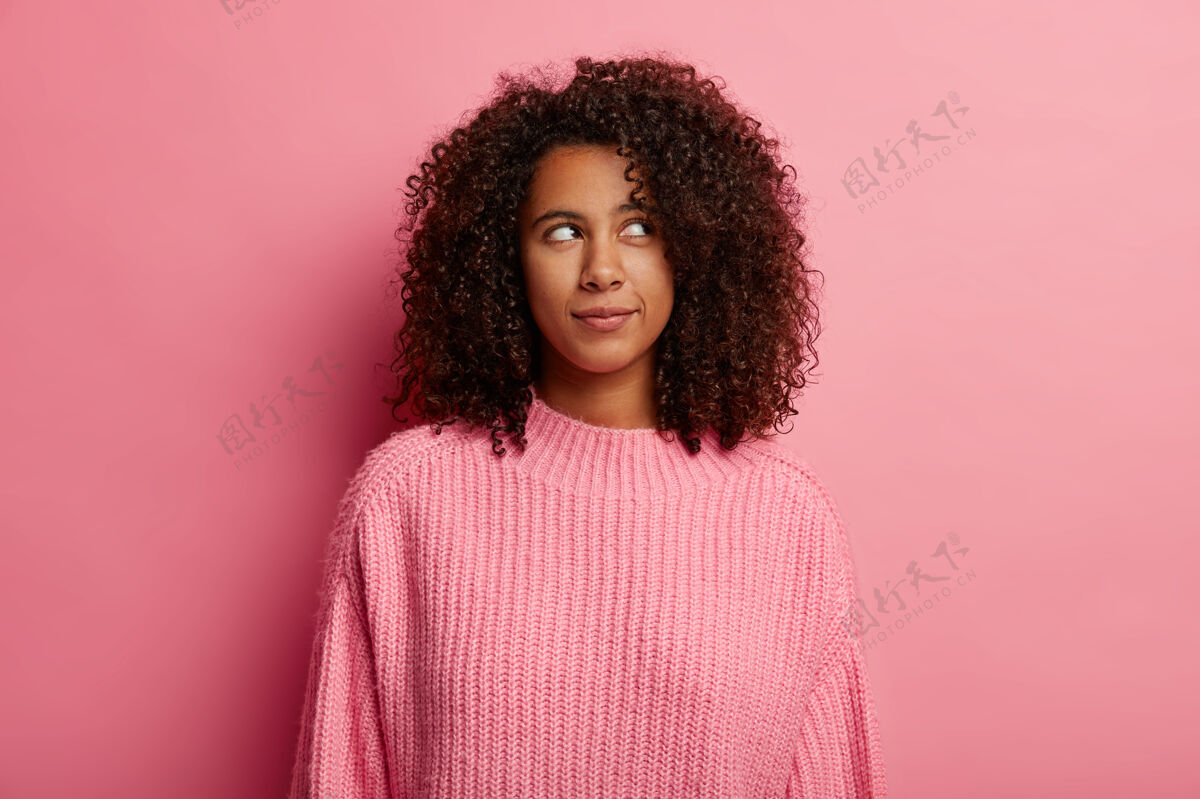 发型迷人的非洲裔少女在右上角若有所思地看着 有着深思熟虑的表情 穿着粉色毛衣 在室内摆姿势 怀疑什么女朋友年轻表情
