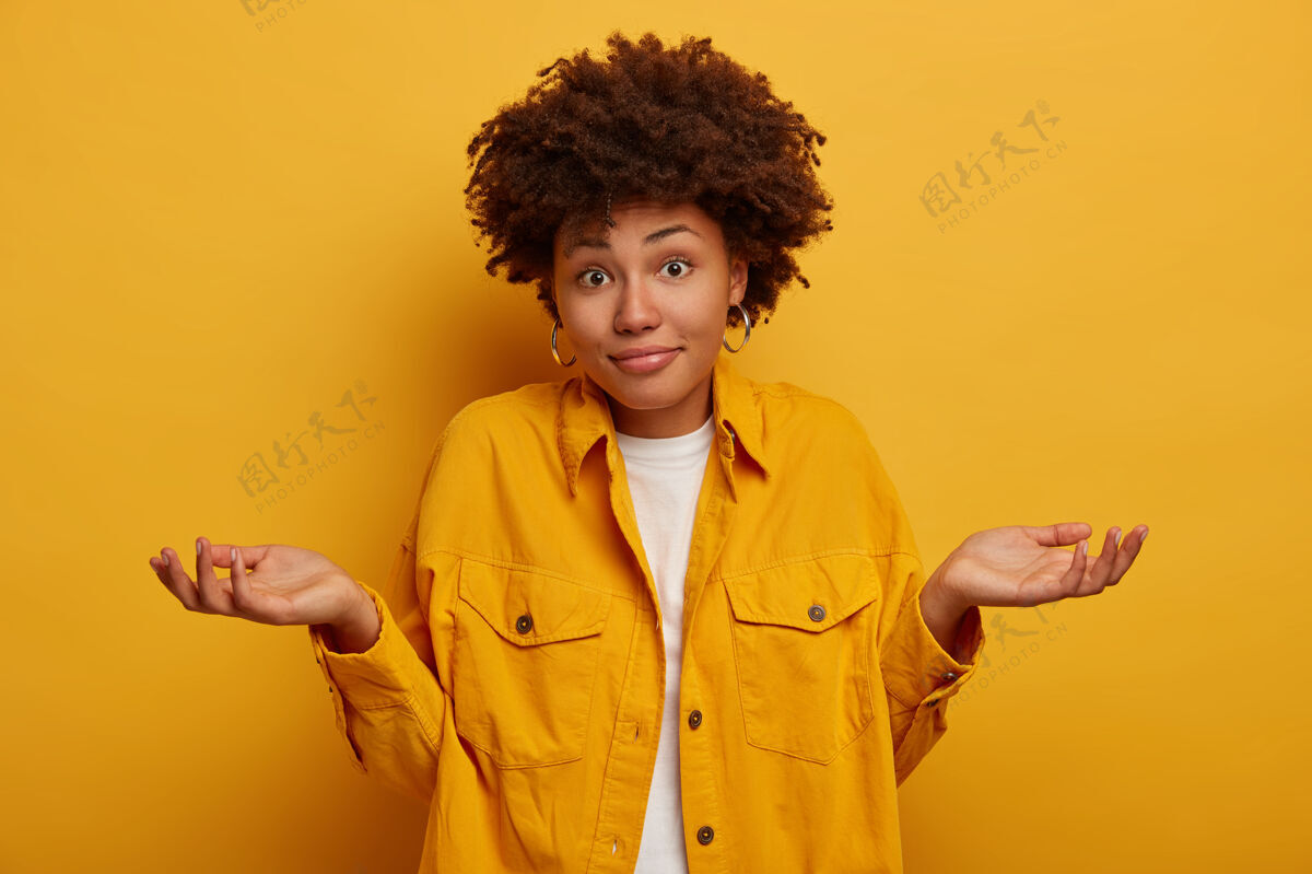 肖像非洲女人耸耸肩 表示不确定 做决定 穿着时髦的衣服 把手掌侧放在黄色的墙上女人人看