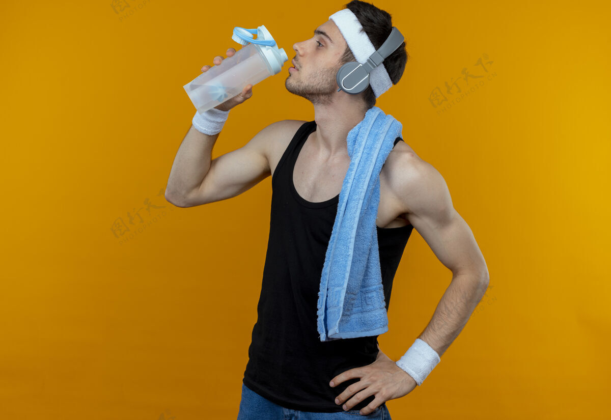 周围戴着头巾的年轻运动型男子 脖子上缠着毛巾 运动后在橘子上滴水运动水站