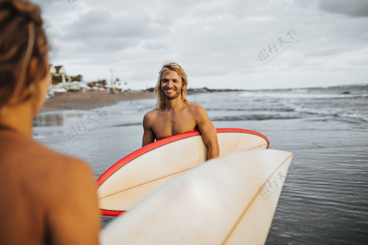 冲浪板长发男人微笑着看着女孩这对夫妇要去冲浪了成人男人海洋